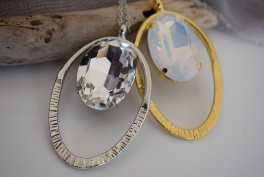 Andromeda Necklace With Crystal – Greek Hammered Jewelry – 18K Gold, Silver, or Rose Gold Plated. Oval hammered pendant with luminous crystal centerpiece.