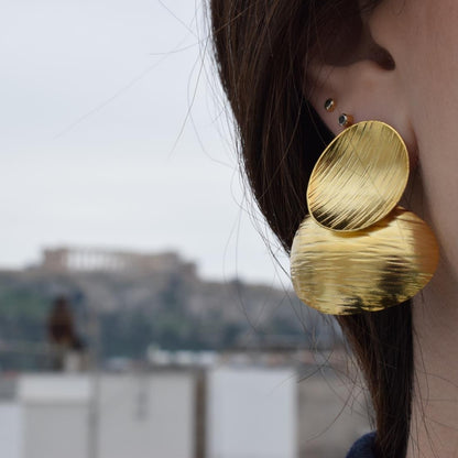 Ostraka earrings – Greek hammered jewelry with bold round textured discs, inspired by ancient Greek pottery shards, available in 18K gold-plated, 18K silver-plated, and rose-gold plated finishes.